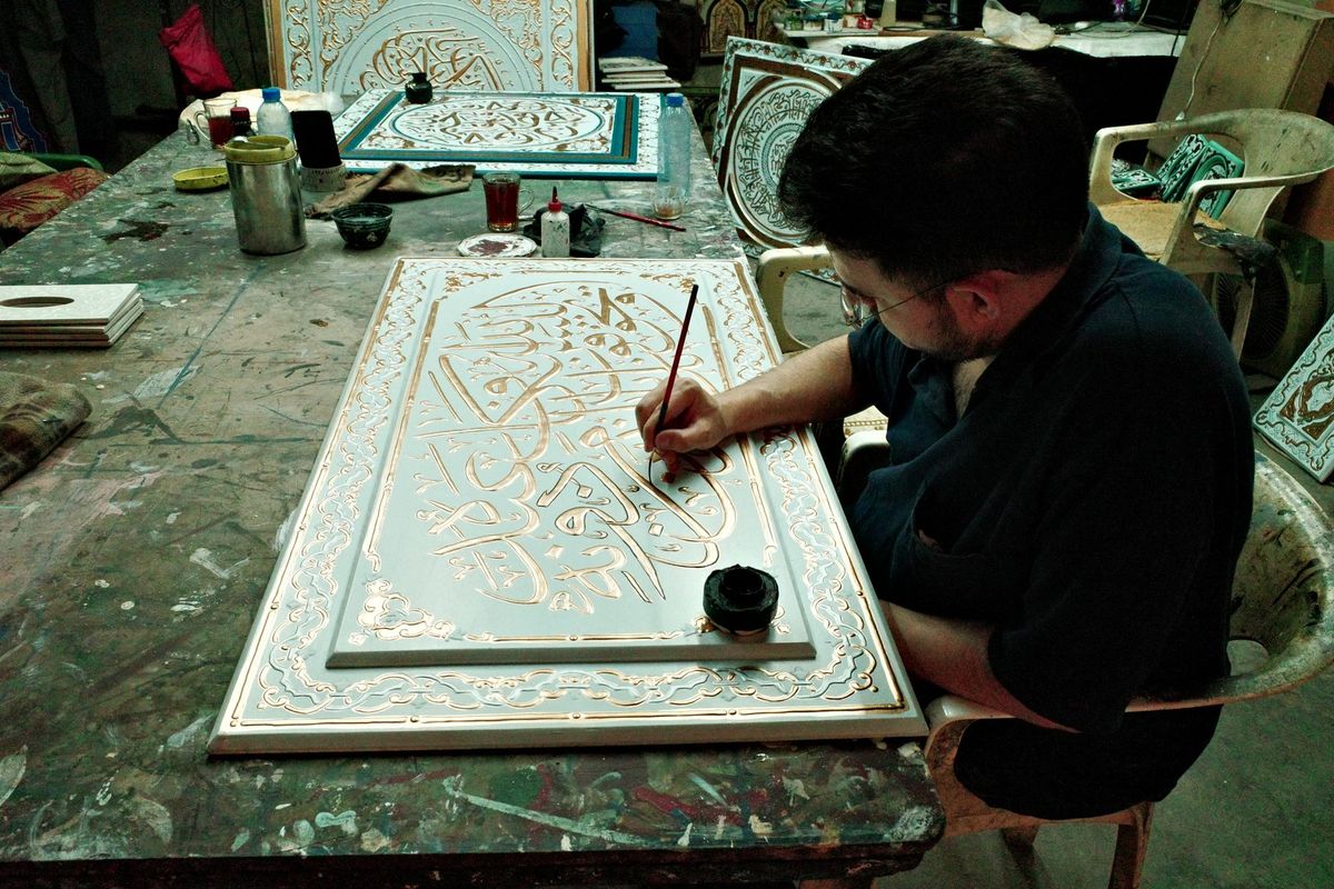 Artisan appliquant avec précision une décoration dorée sur un panneau en bois à l'aide d'un pinceau fin