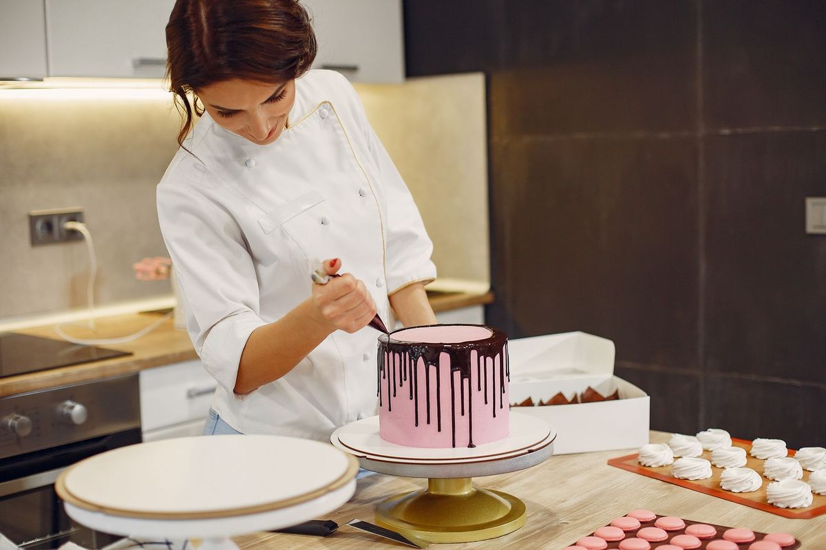 Pâtissière appliquant des coulures de chocolat sur un gâteau avec précision dans sa cuisine professionnelle