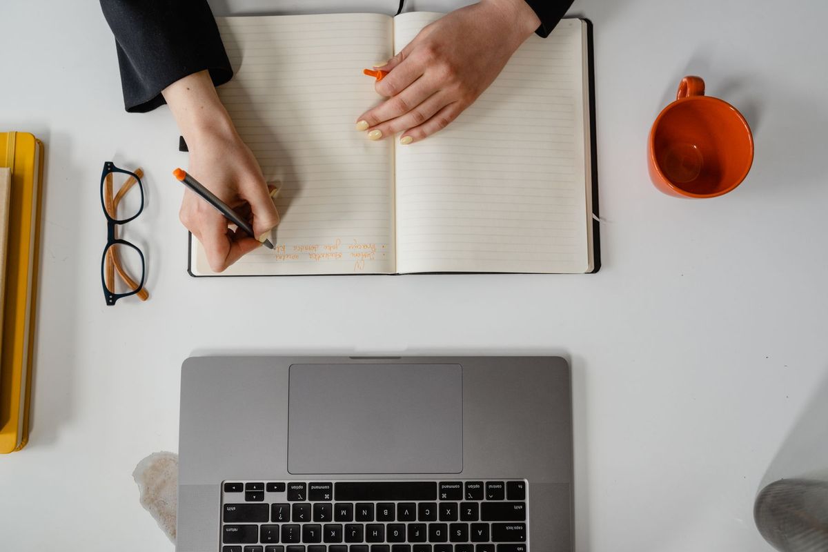 Femme copywriter notant ses idées dans un carnet à côté de son ordinateur portable