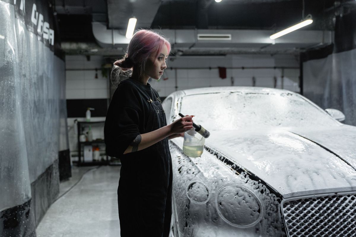 Femme nettoyant une voiture avec de la mousse dans un centre de lavage automobile professionnel