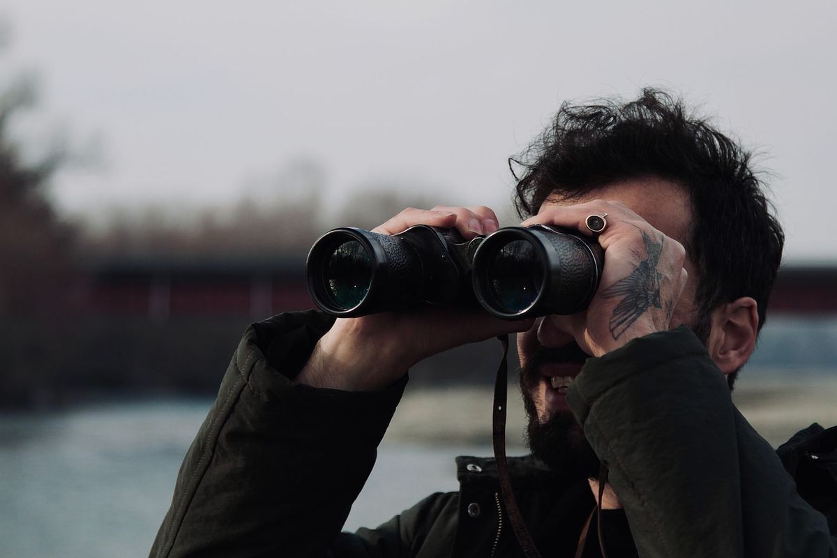 Homme observant à travers des jumelles près d'une rivière pour une enquête