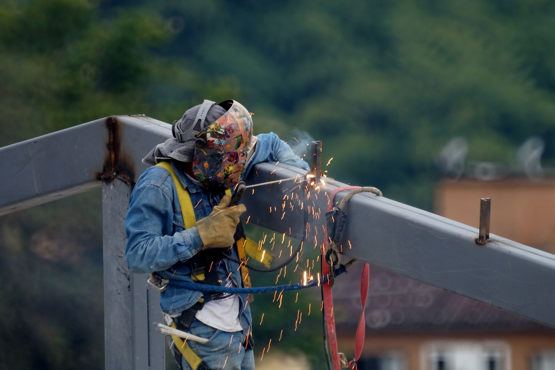 Ouvrier en équipement de sécurité soudant une poutre d'acier avec projection d'étincelles sur un chantier