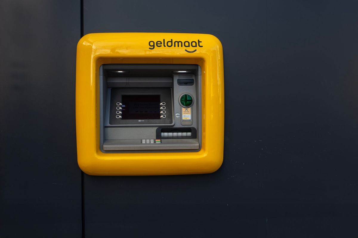 Distributeur automatique de billets jaune vif encastré dans un mur, symbolisant les transactions en espèces sécurisées