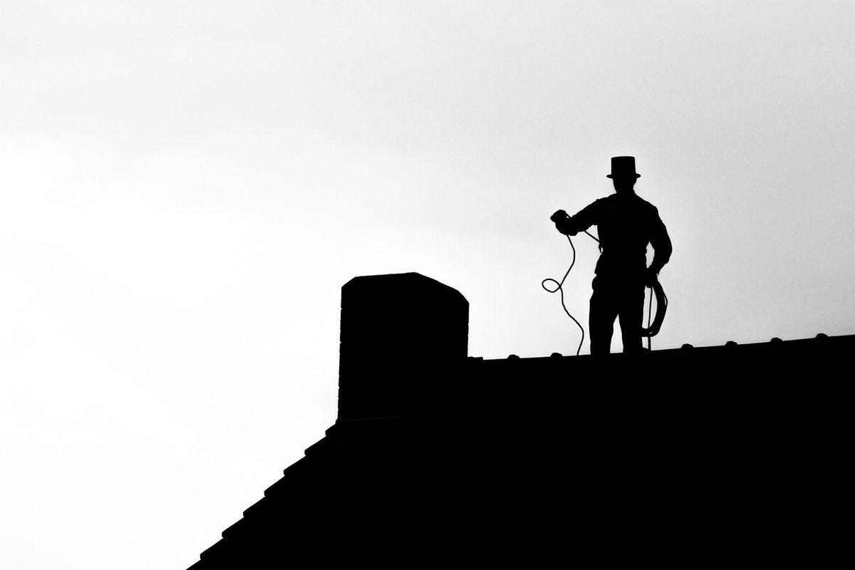 Silhouette d'un ramoneur avec son balai sur un toit près d'une cheminée