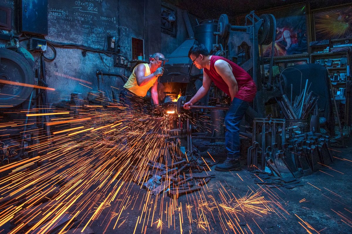 Deux artisans frappent le métal incandescent avec des étincelles jaillissantes dans leur atelier
