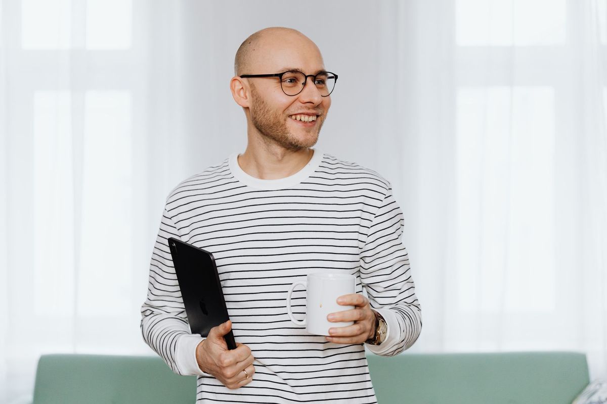 Homme souriant tenant une tablette et une tasse de café à son bureau