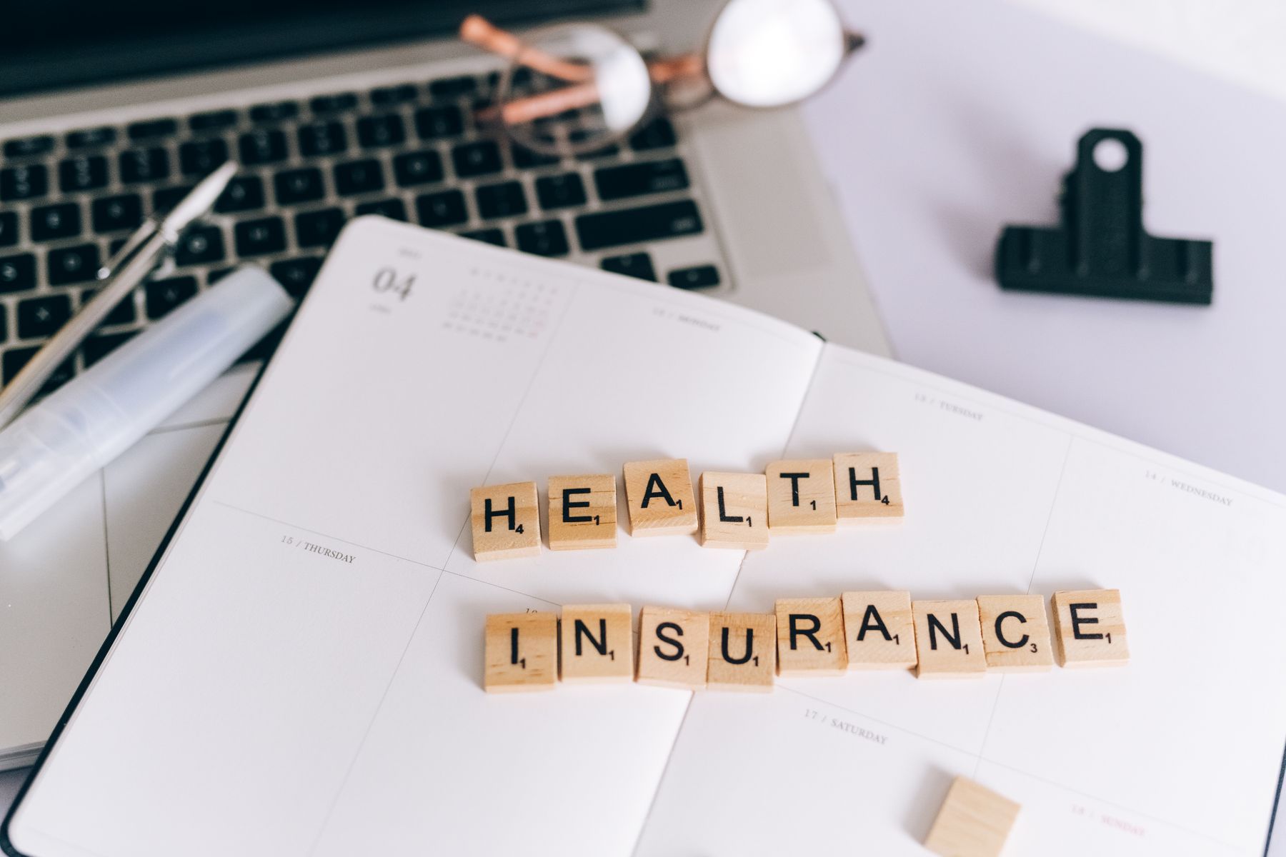 Lettres de Scrabble formant « Assurance Santé » sur un planificateur à côté d'un ordinateur portable