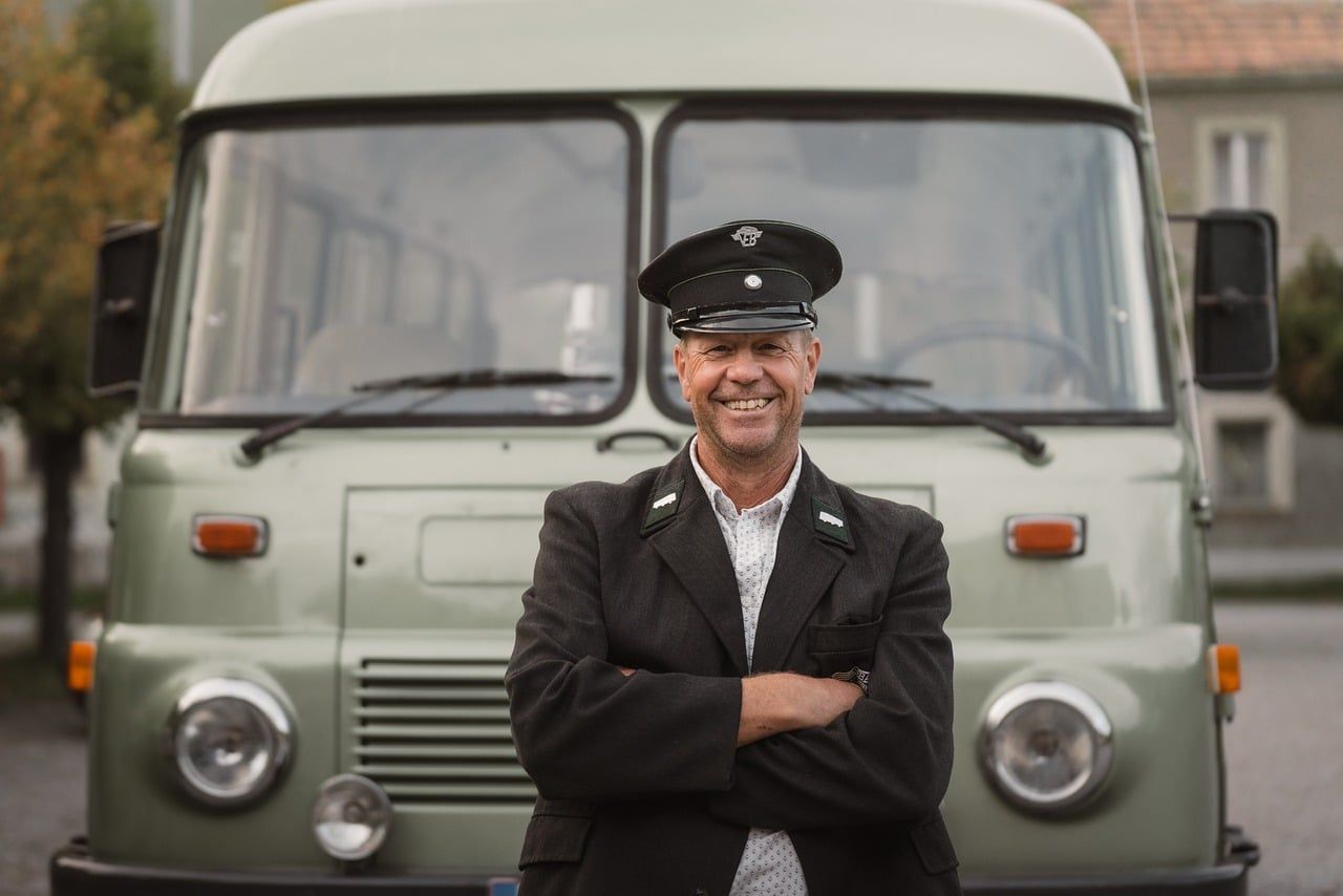 Chauffeur souriant en uniforme devant un van vintage gris dans une rue urbaine