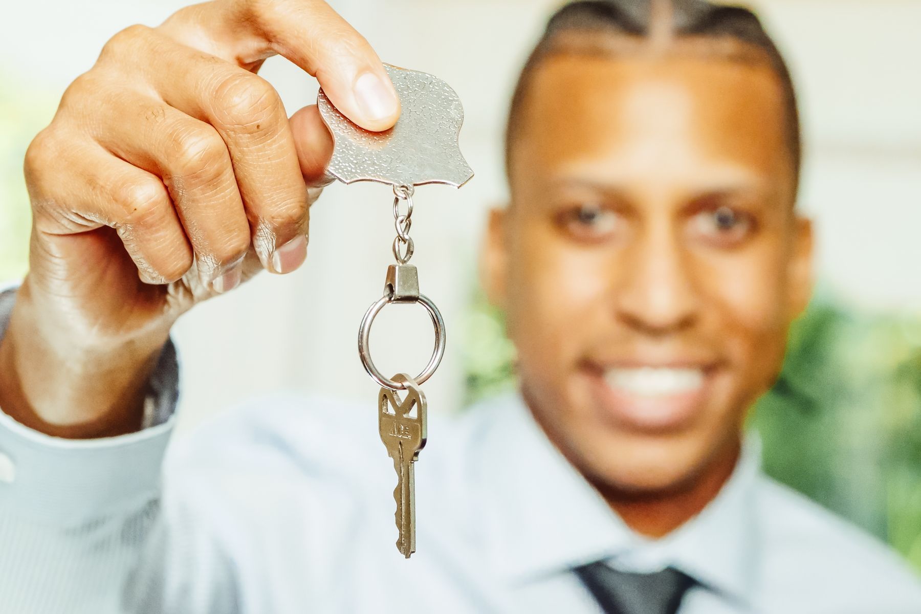 Agent immobilier souriant tenant une clé dorée devant une maison