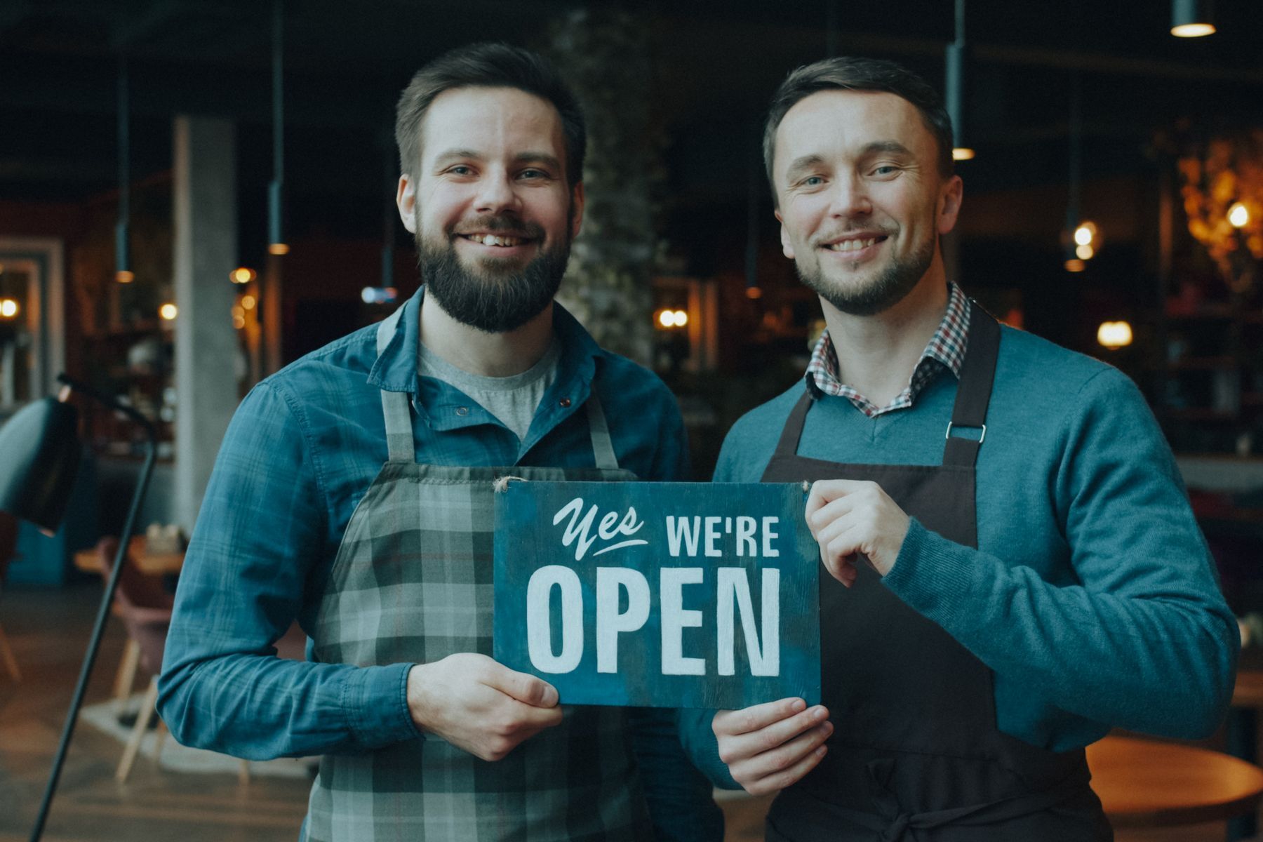 Deux entrepreneurs sourient en tenant une pancarte « Oui, nous sommes ouverts » dans leur café