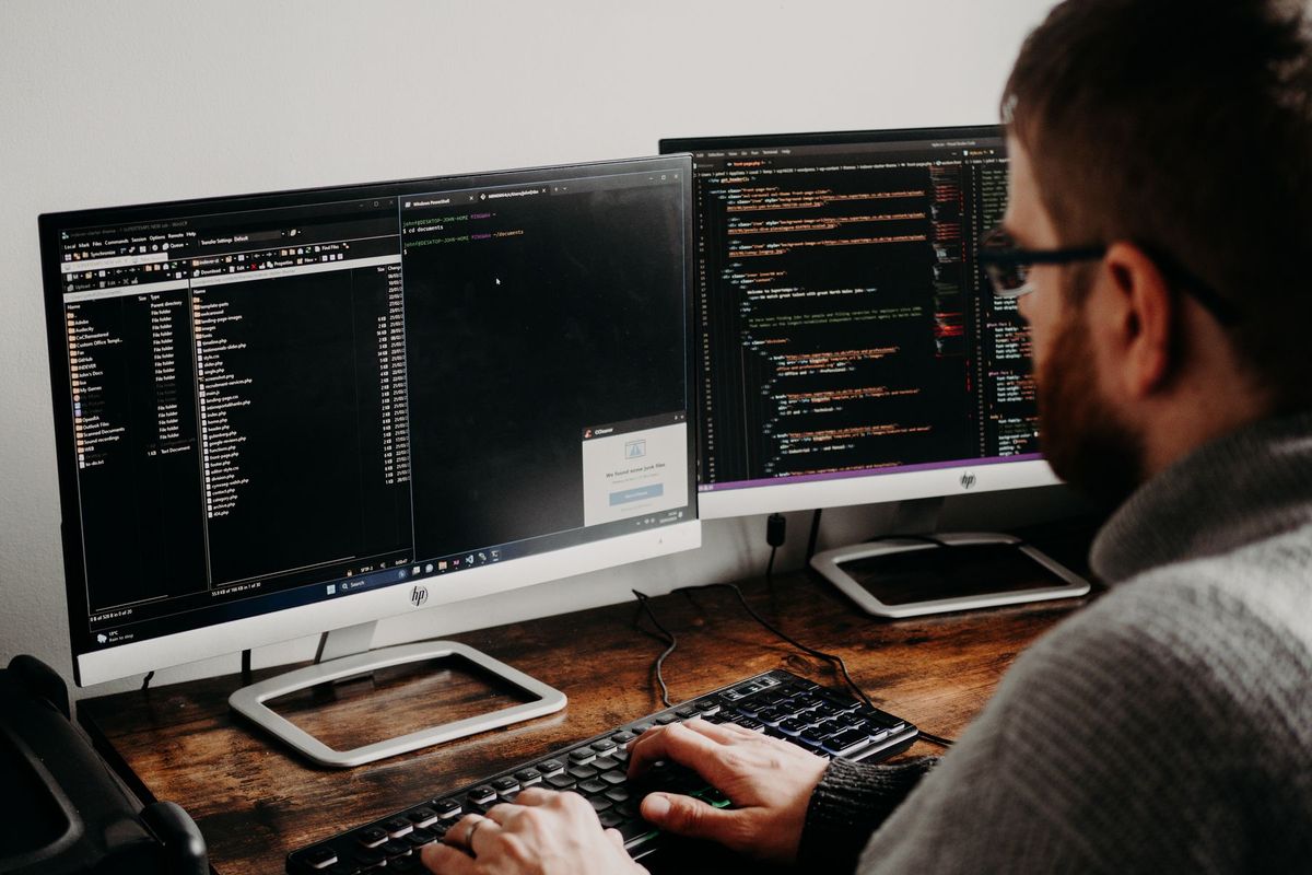 Développeur tapant du code sur deux écrans dans un environnement de travail professionnel