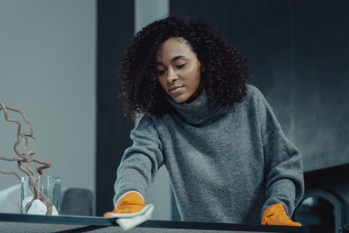 Femme en pull gris nettoyant une table avec un chiffon blanc