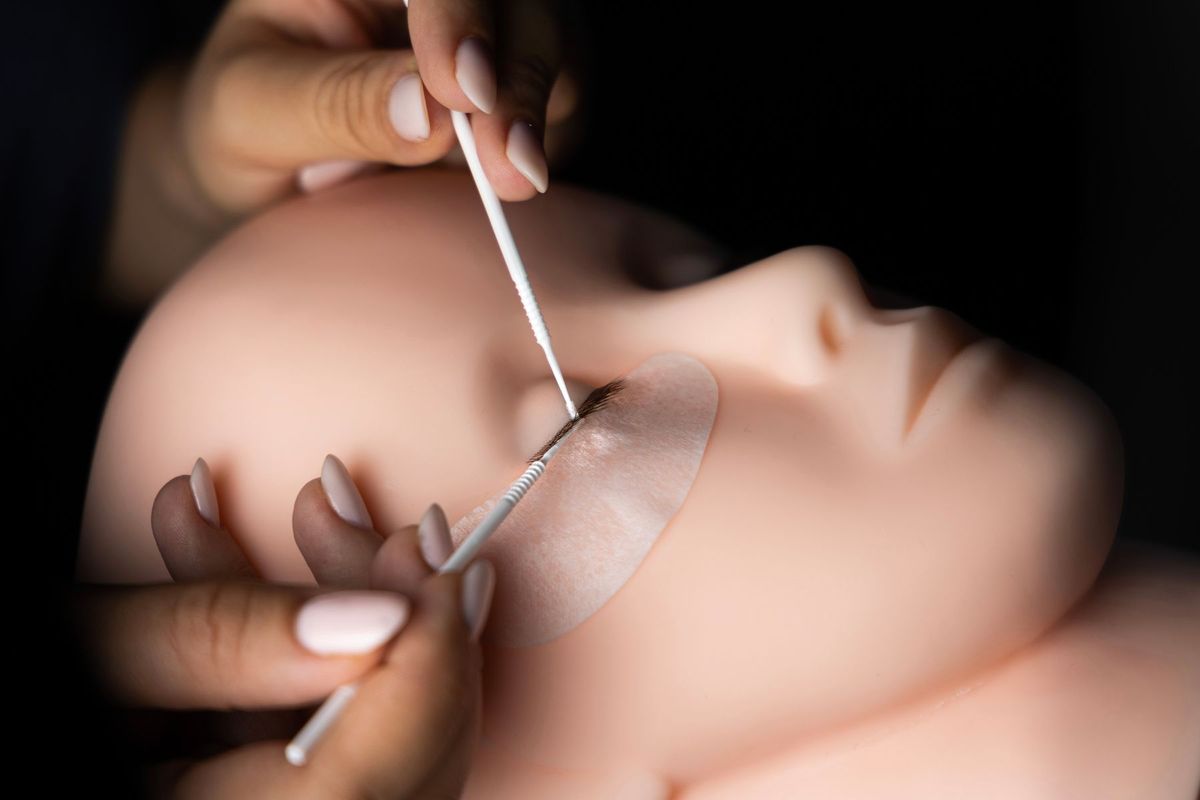 Esthéticienne appliquant des extensions de cils sur un mannequin avec des pinces de précision