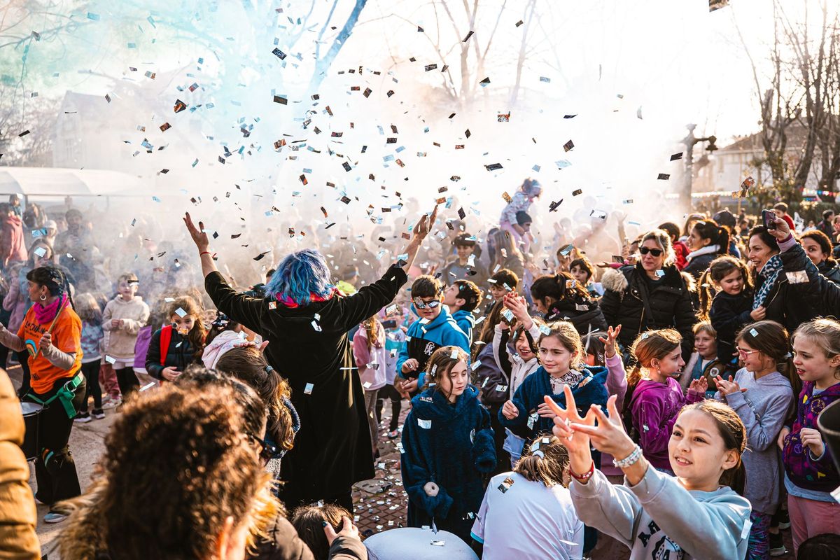 Des enfants rient en levant les bras sous une pluie de confettis colorés lors d'une animation festive en plein air