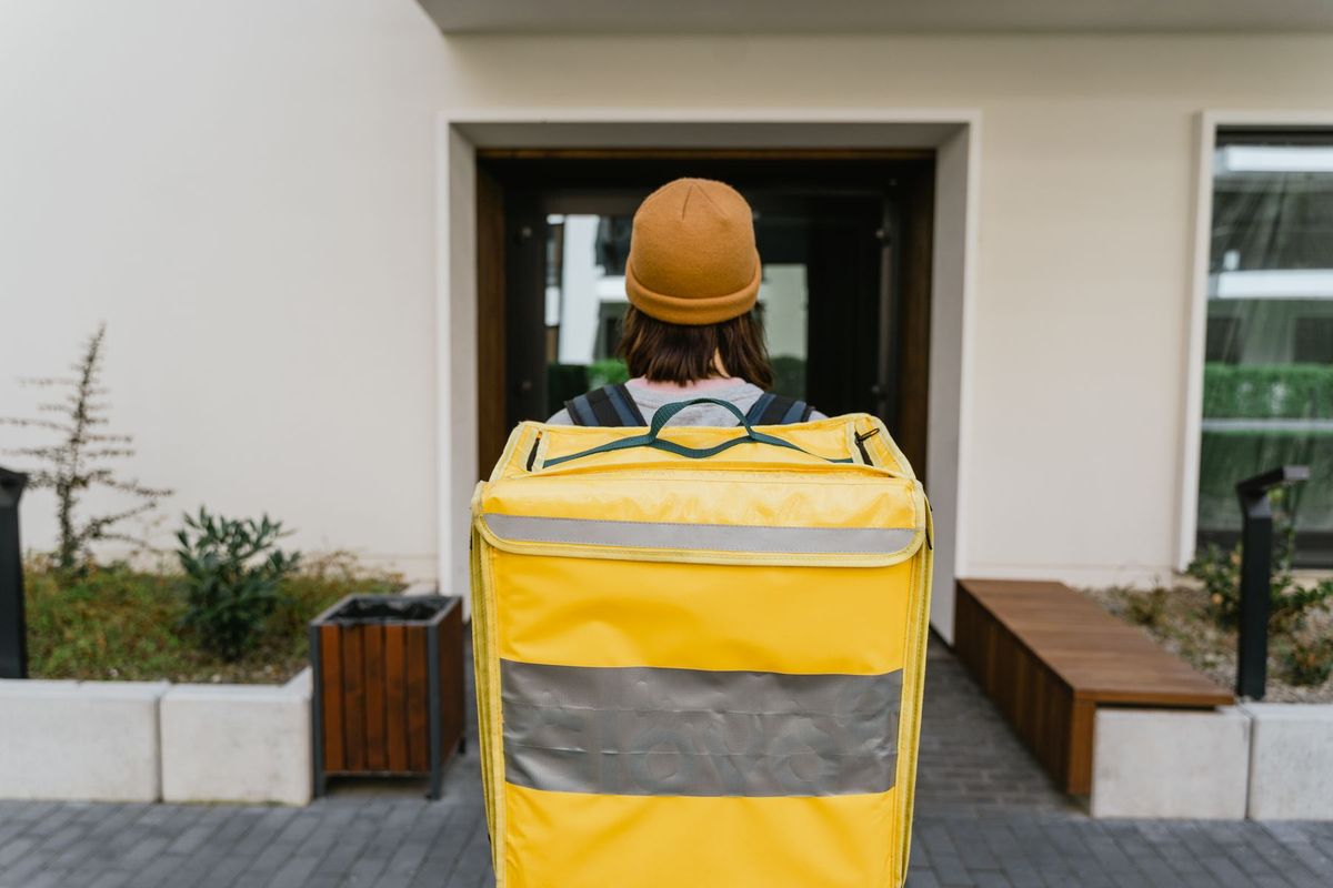 Livreur portant un sac à dos isotherme rouge approchant d'une porte d'immeuble moderne