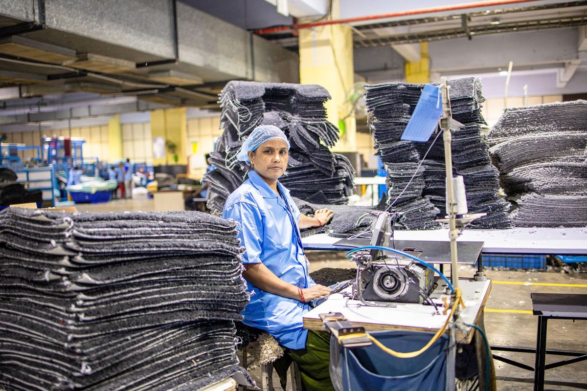 Ouvrier en atelier posant ses mains sur une machine à coudre industrielle entourée de rouleaux de moquette