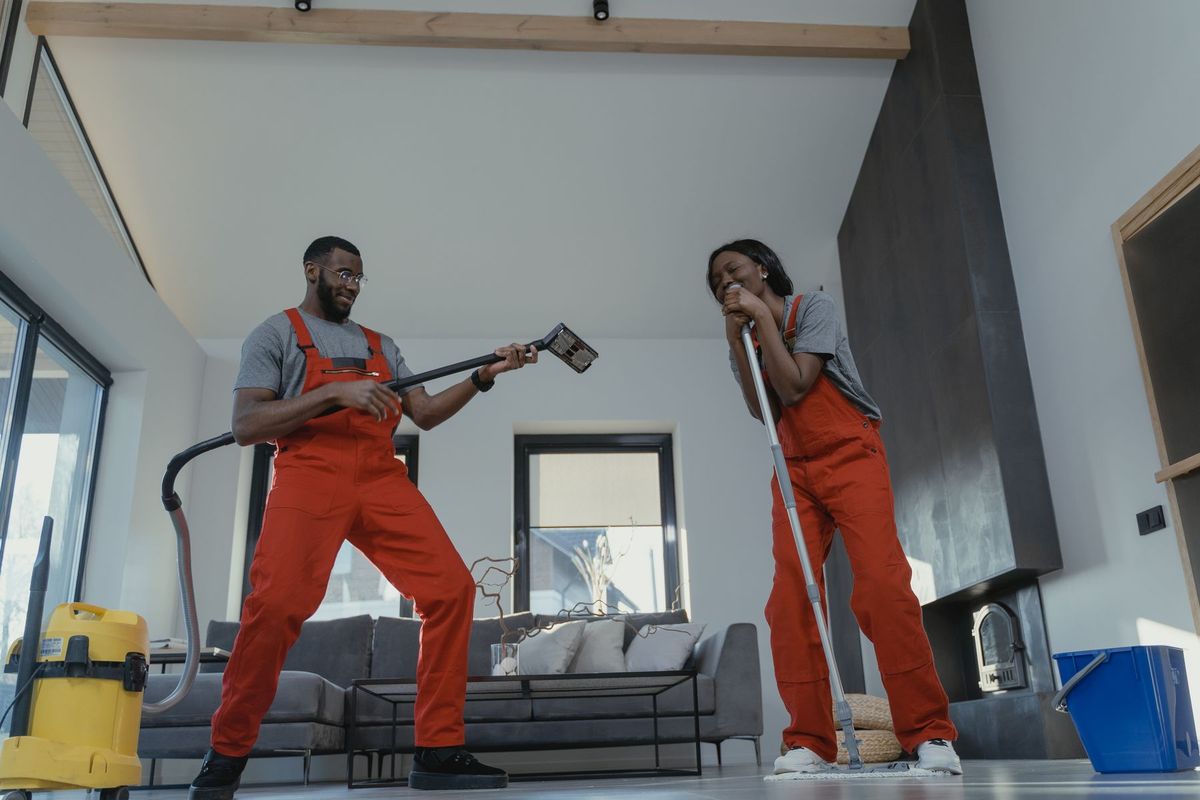 Deux agents de nettoyage en tenue professionnelle rouge utilisent aspirateur et serpillère dans un intérieur