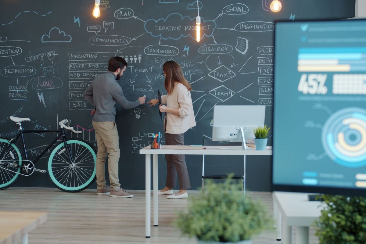 Deux entrepreneurs discutent devant un tableau noir rempli de schémas et de stratégies