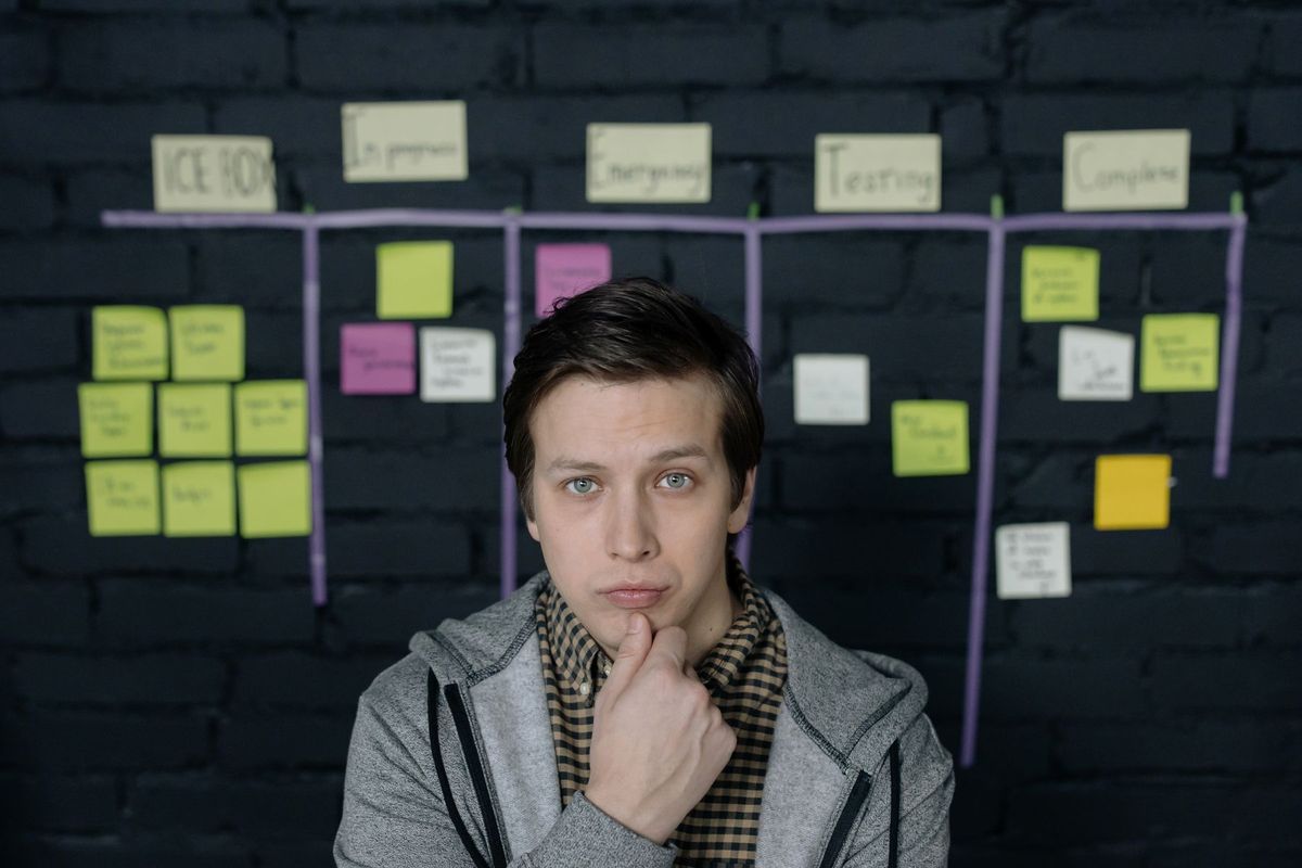 Homme observant un tableau de projet avec des tâches et des post-its dans un espace de travail collaboratif