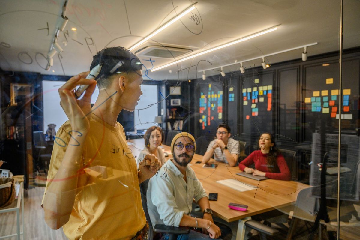 Équipe de professionnels discutant stratégie autour d'un tableau blanc en verre