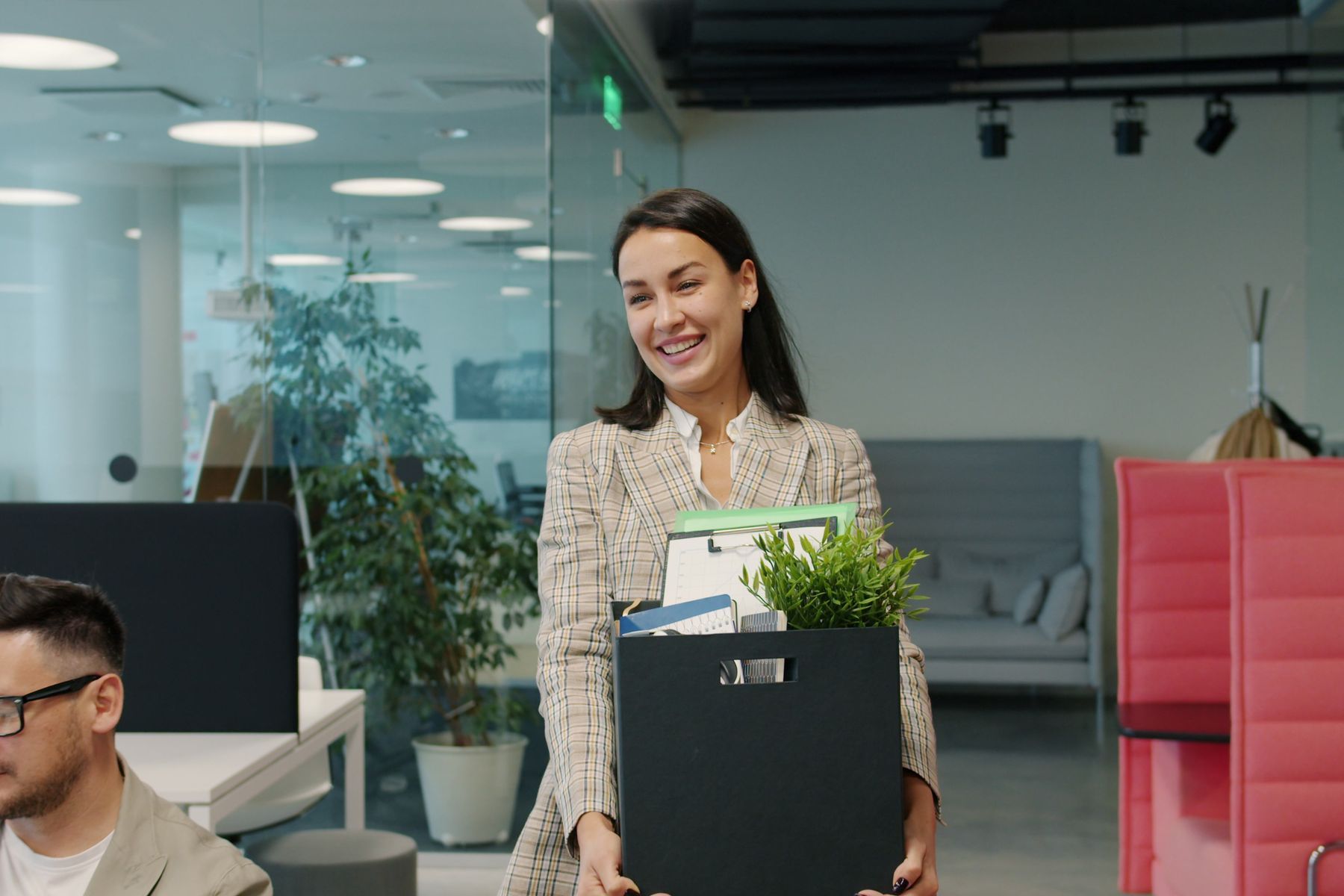 Femme d'affaires souriante transportant ses affaires et une plante verte dans un bureau moderne