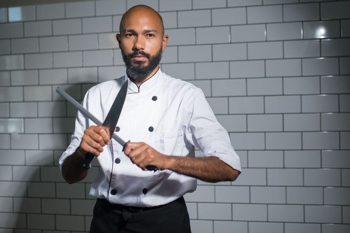Chef aiguisant précisément son couteau sur une pierre à aiguiser en cuisine professionnelle