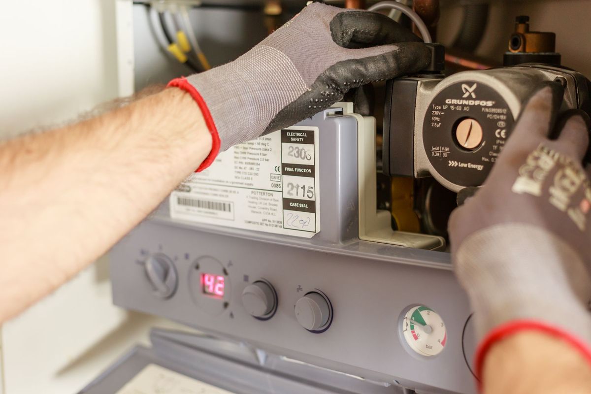 Mains d'un chauffagiste réglant une chaudière avec des outils de précision