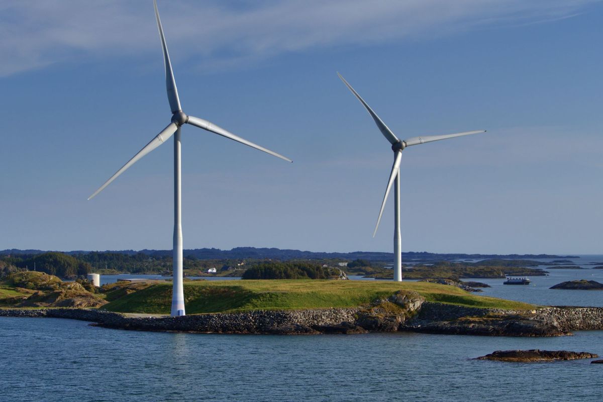Deux éoliennes blanches tournent sur une île côtière sous un ciel bleu dégagé