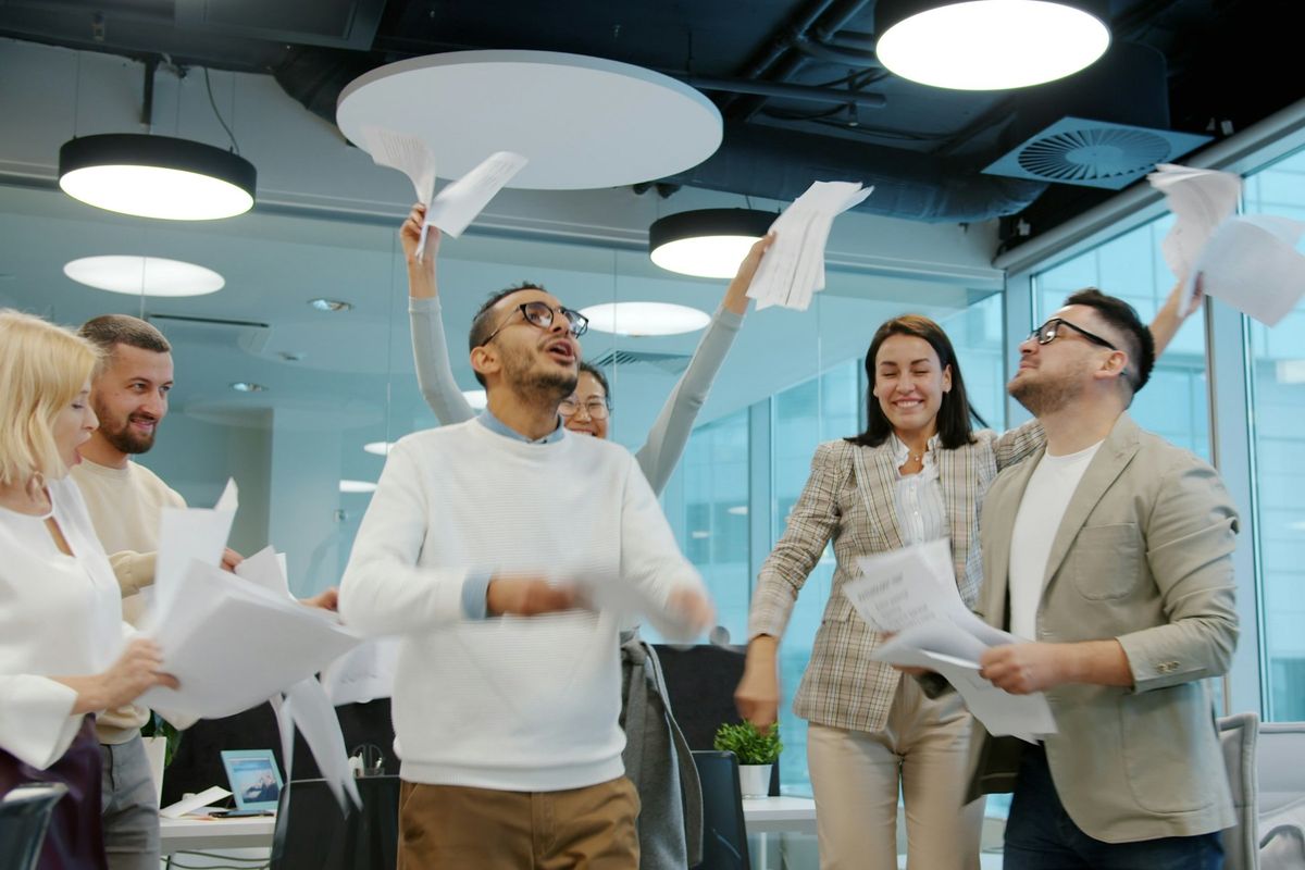 Équipe diversifiée célébrant une victoire en jetant des papiers dans un bureau