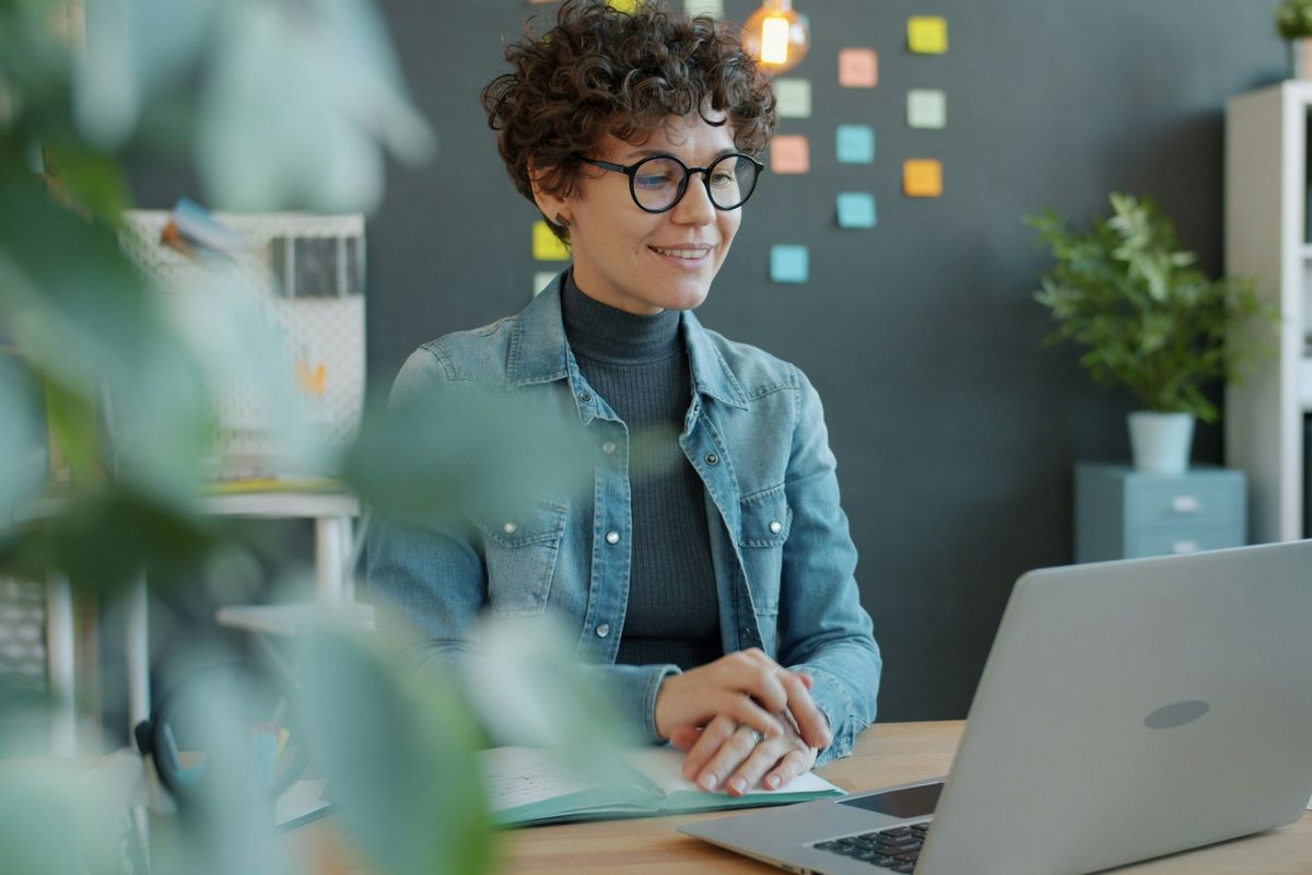 Femme souriante aux cheveux bouclés travaillant sur son ordinateur portable