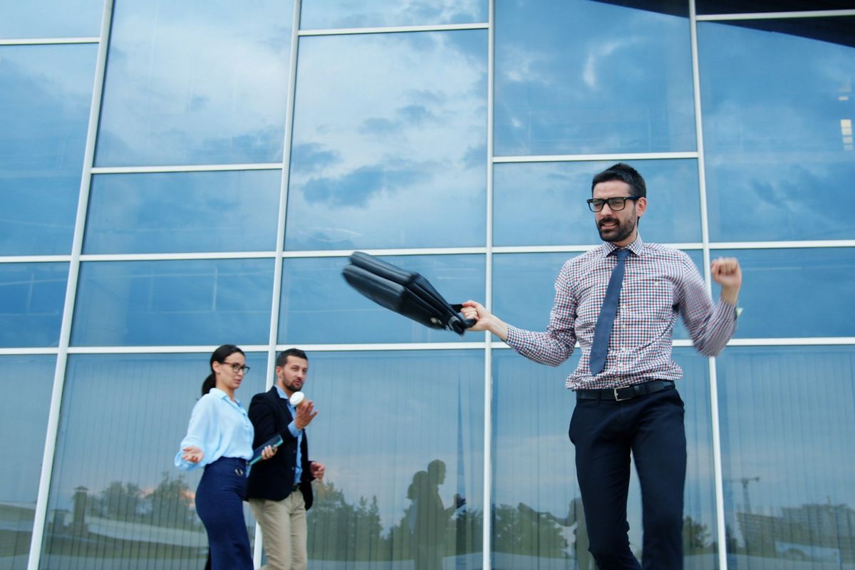 Homme en costume levant les bras de joie devant un immeuble de bureaux moderne