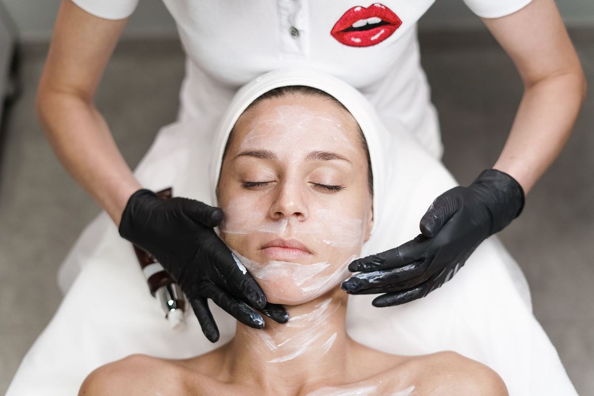 Esthéticienne appliquant un masque de soin sur le visage d'une cliente allongée dans un cadre apaisant