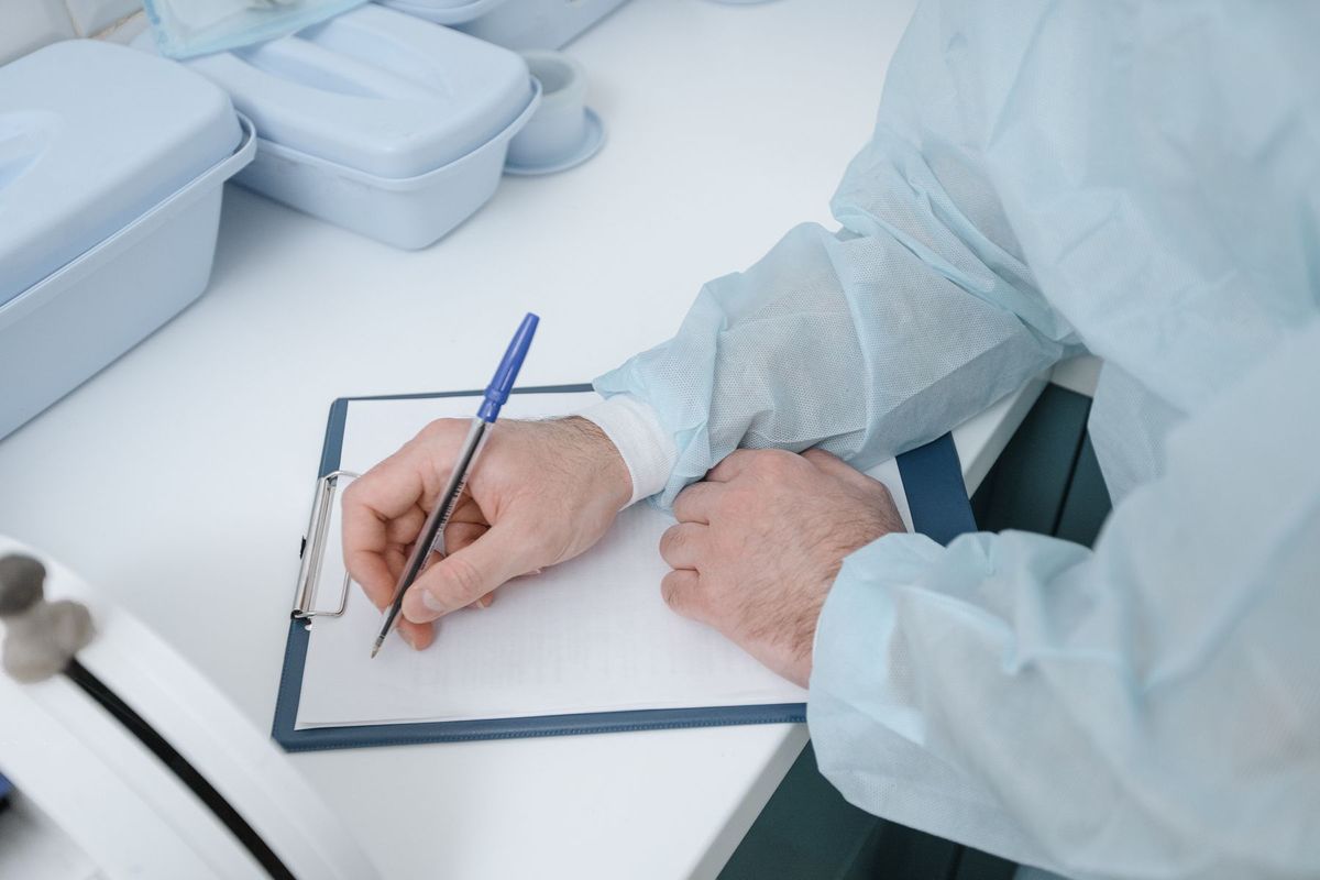Médecin en blouse blanche et masque chirurgical notant des observations sur un dossier patient