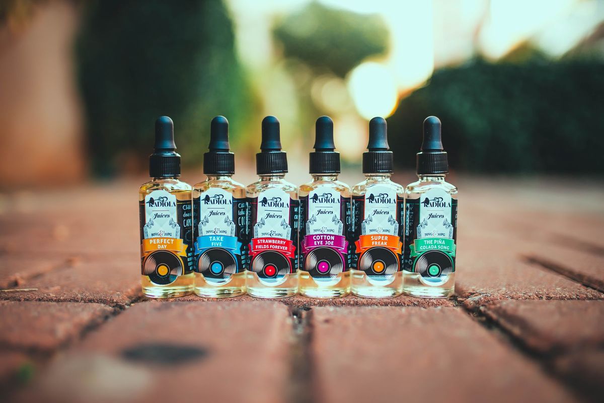 Bouteilles de e-liquide colorées alignées sur un chemin en briques devant un commerce