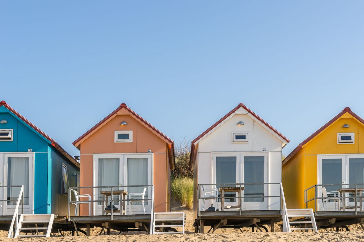 Rangée de petits bungalows colorés alignés sur une plage de sable blanc sous un ciel bleu dégagé