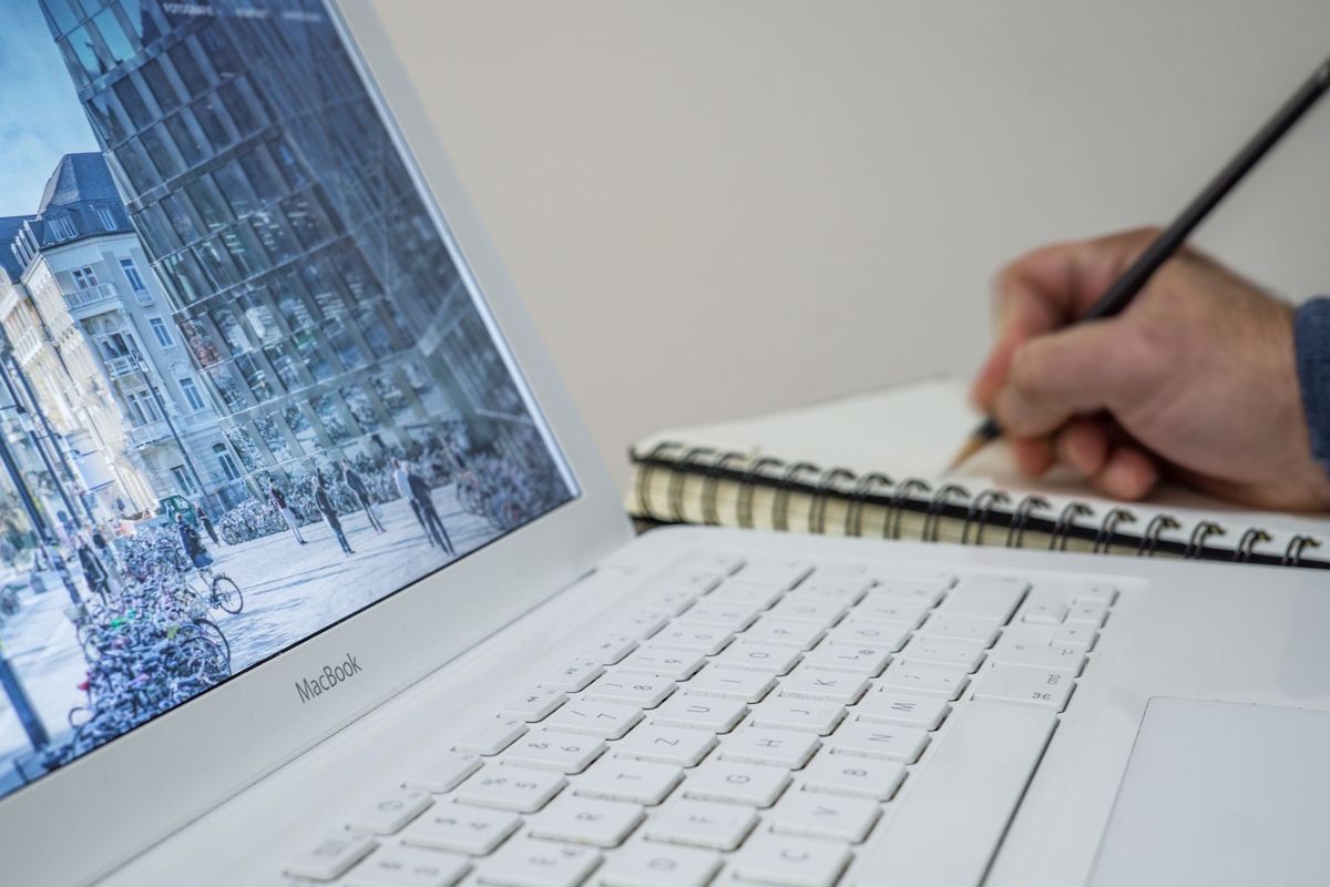 Un rédacteur web prenant des notes dans un cahier à côté de son ordinateur portable