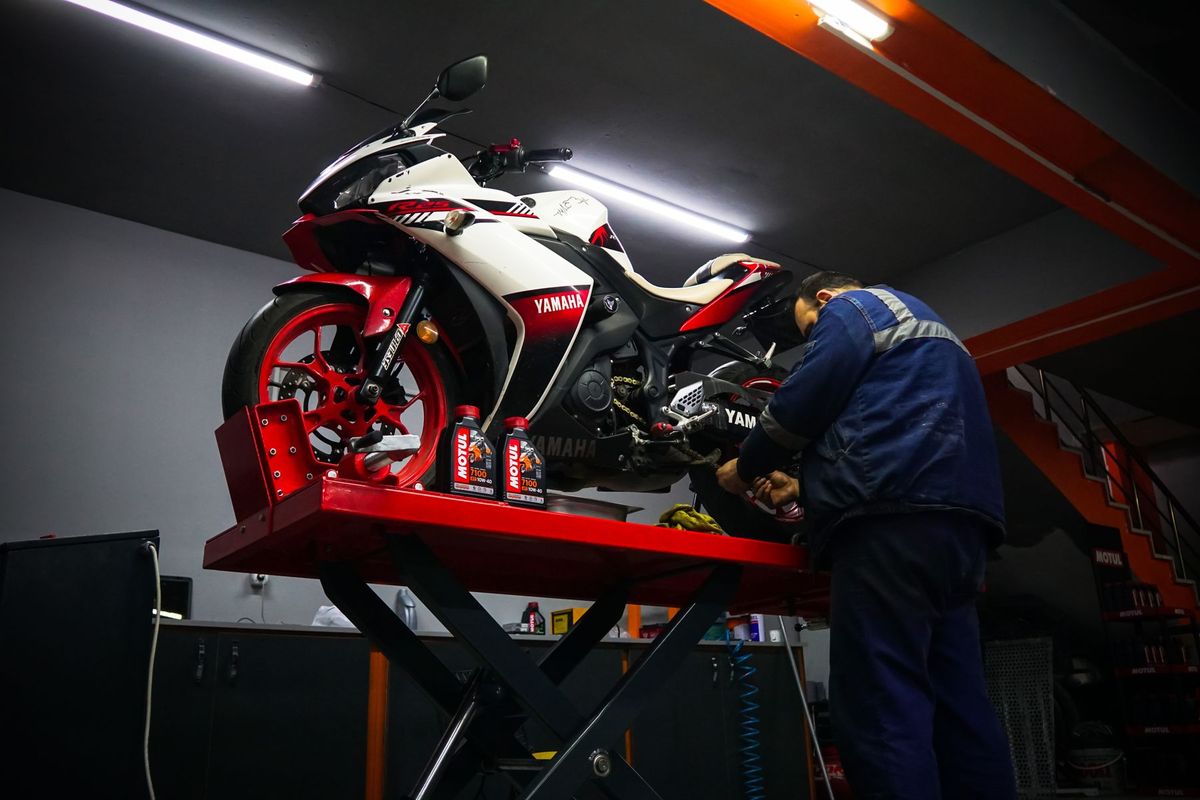 Mécanicien en bleu de travail réparant le moteur d'une moto dans un garage équipé
