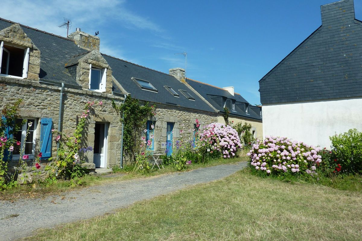 Maison en pierre avec volets noirs et toiture en tuiles brunes