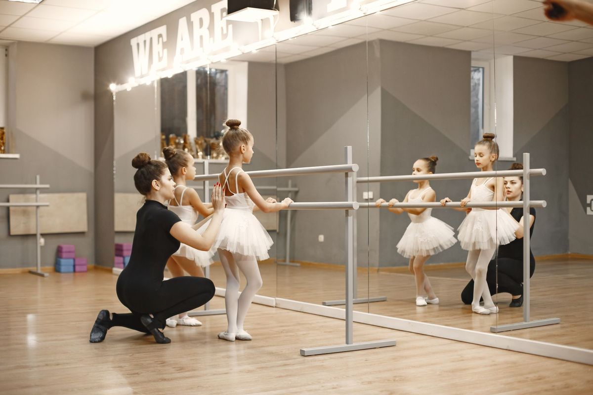 Professeur de danse guidant des élèves en tutus lors d'un exercice à la barre
