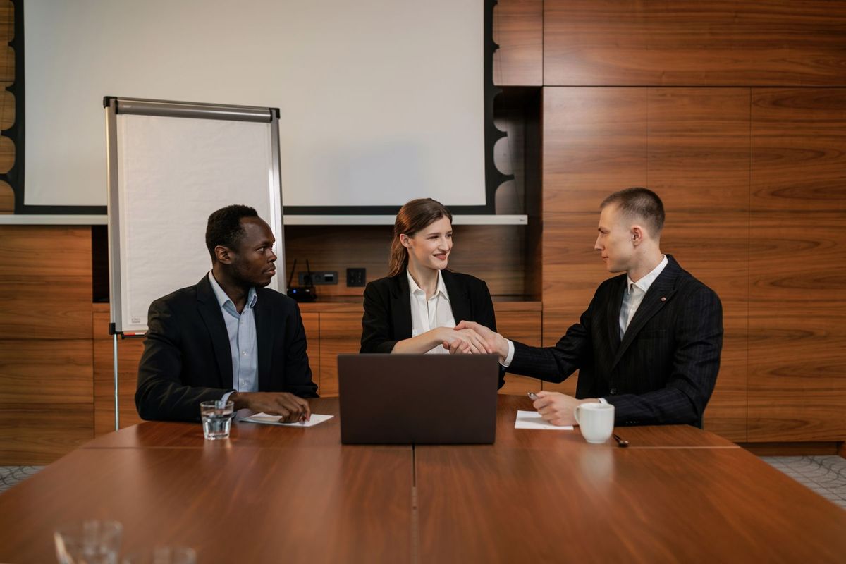 Trois entrepreneurs se serrent la main autour d'une table de réunion dans un bureau moderne