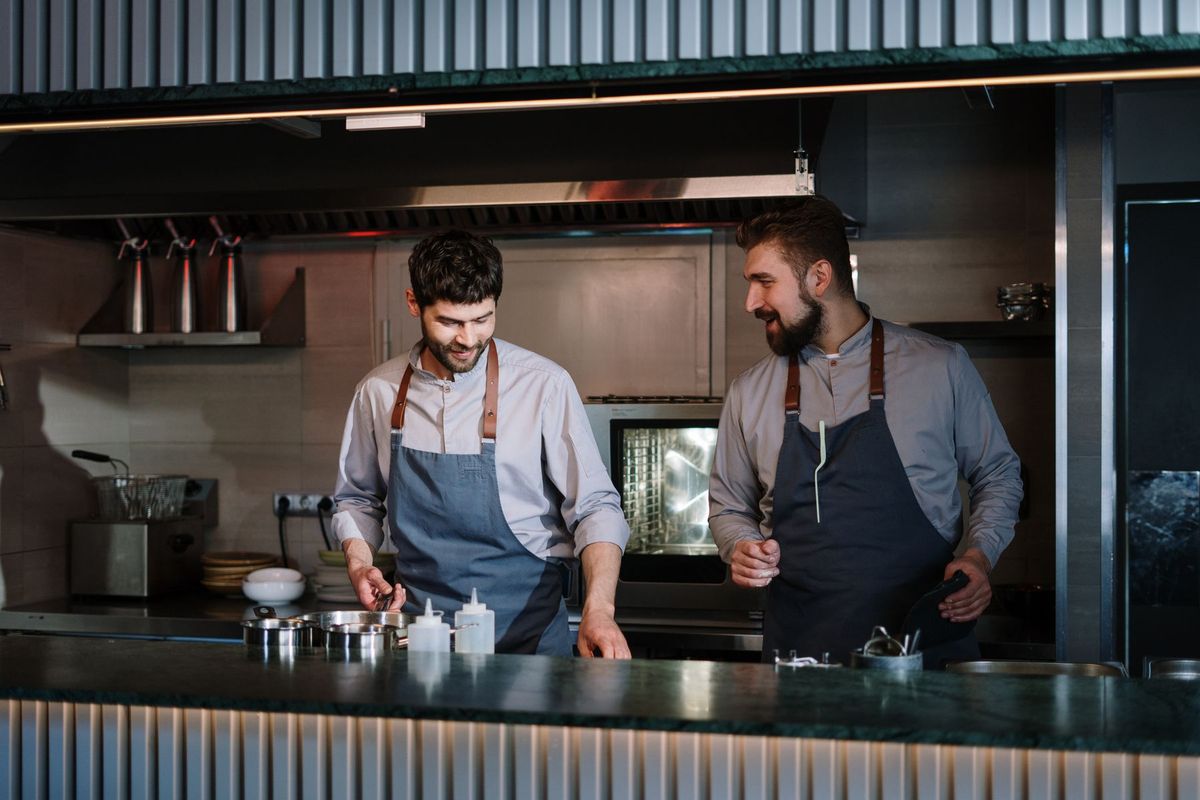 Deux cuisiniers en tenue professionnelle préparent un plat dans une cuisine moderne et équipée