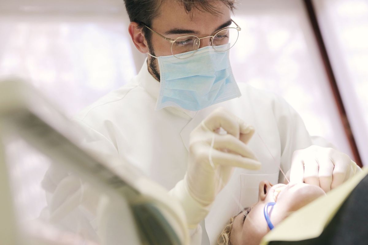 Dentiste en masque effectuant un soin dentaire sur un patient allongé