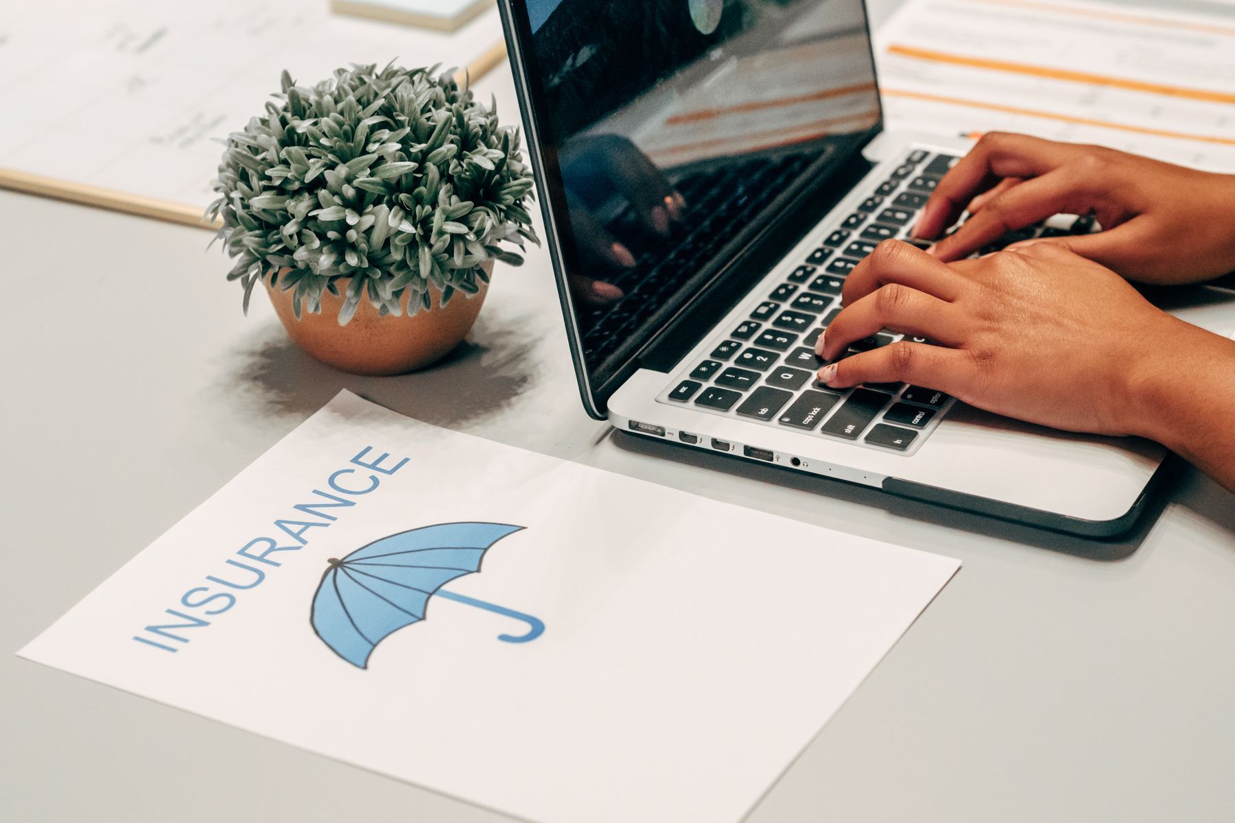Mains tapant sur un clavier d'ordinateur portable avec documents d'assurance et plante sur le bureau