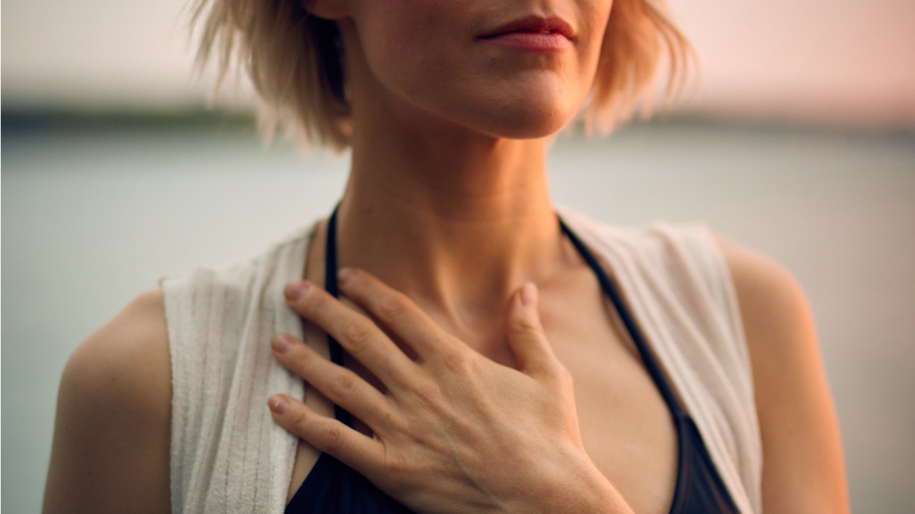 A woman with short blonde hair puts her hand on her chest so she can feel her chest and diaphragm move as she does deep belly breathing.