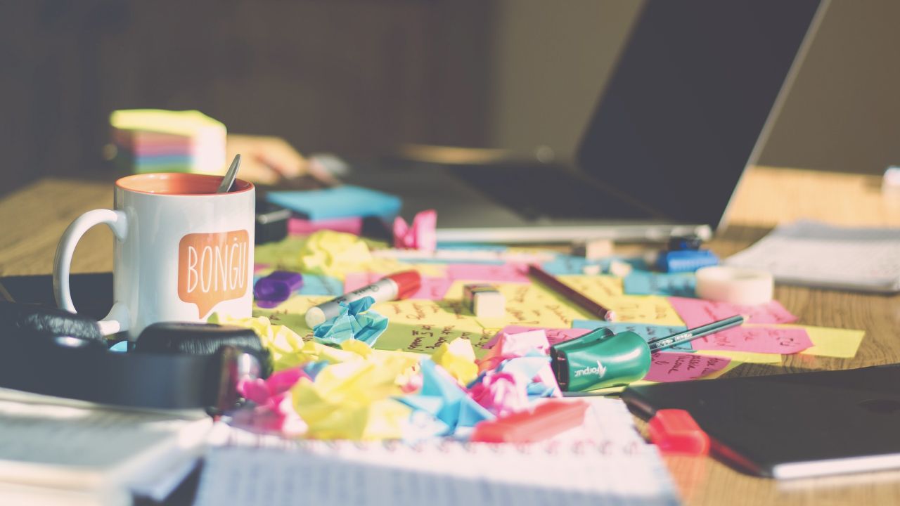 A messy desk with a coffee cup, and multi-coloured crumpled-up sticky notes.