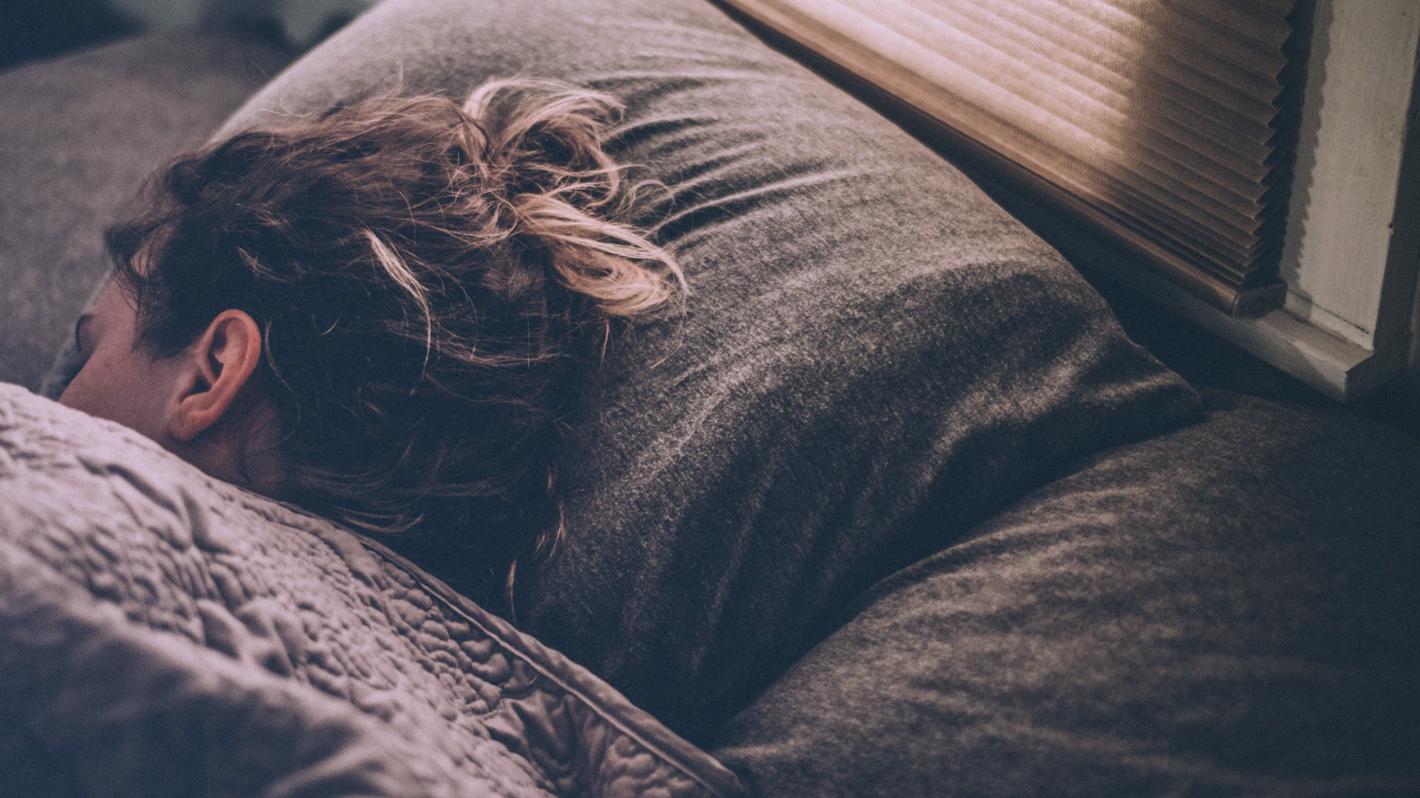 A person with long hair sleeping in a bed with gray flannel sheets--practising gratitude may be good for sleep.