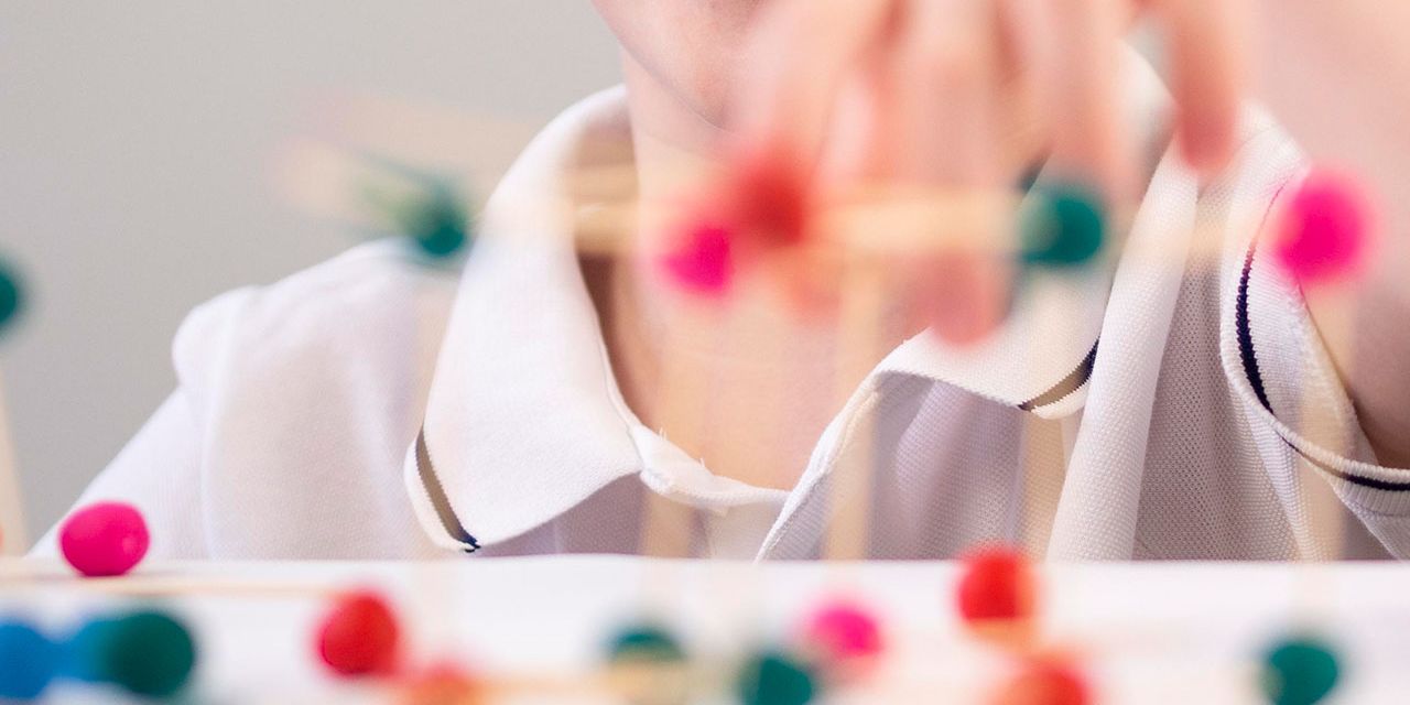Criança sorrindo enquanto brinca com estruturas coloridas feitas de palitos e bolinhas, representando desenvolvimento e estímulo cognitivo.