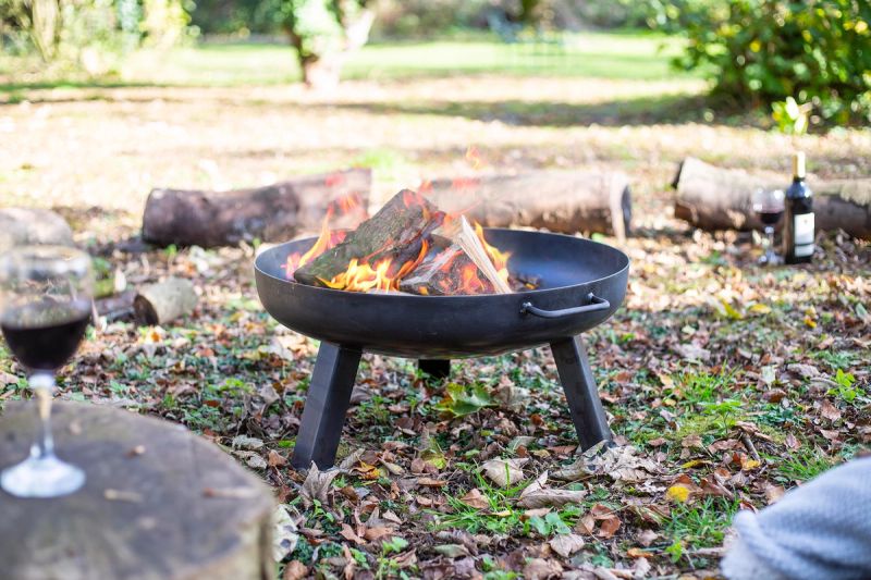 Person sitting next to a lit black round fire pit with red wine