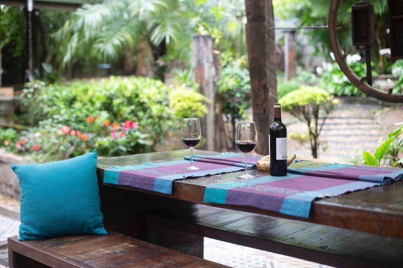 Wooden table with glasses of wine on top and with a garden background