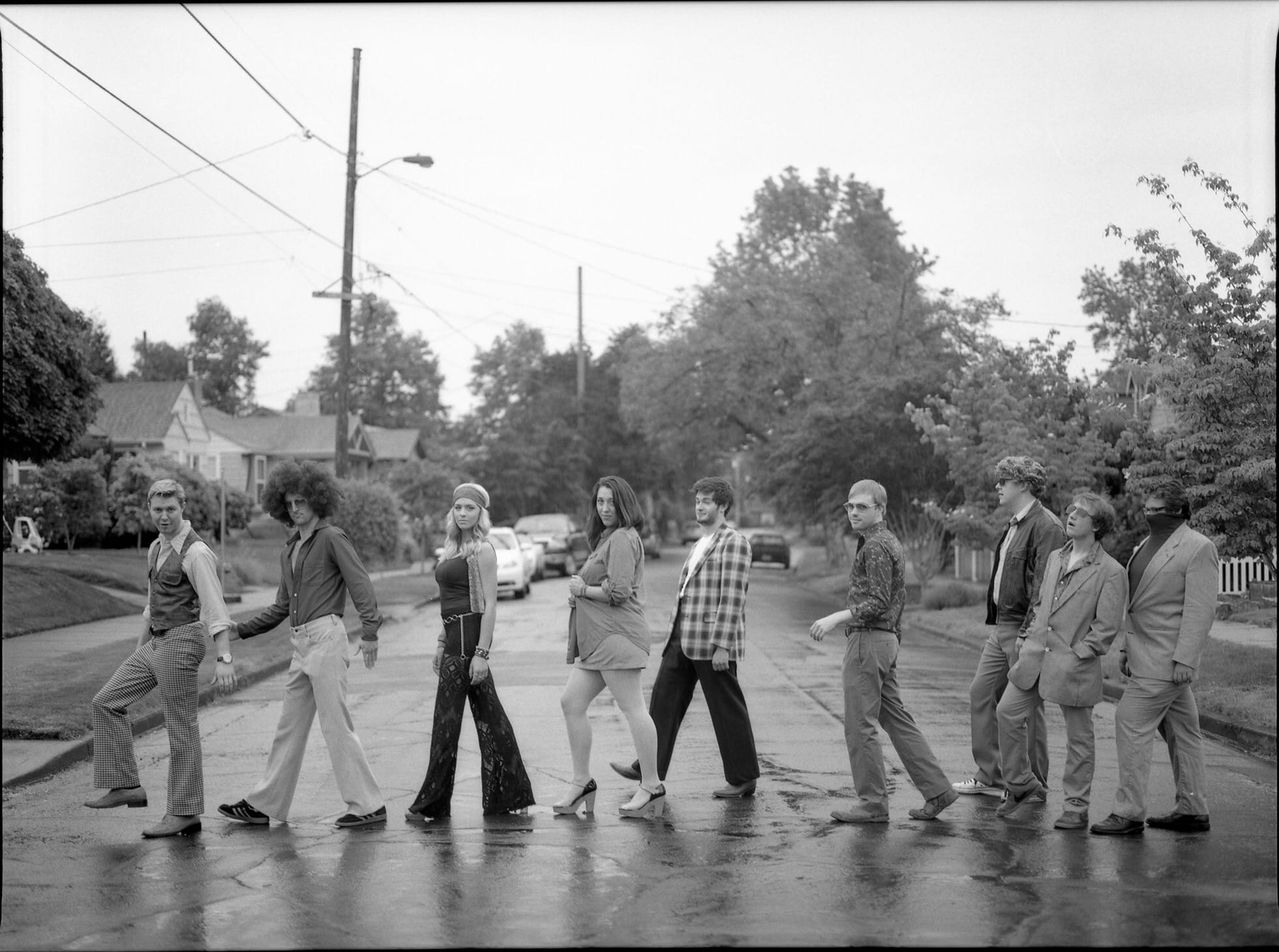 Friends in 1970s outfits crossing a street in a line, black and white